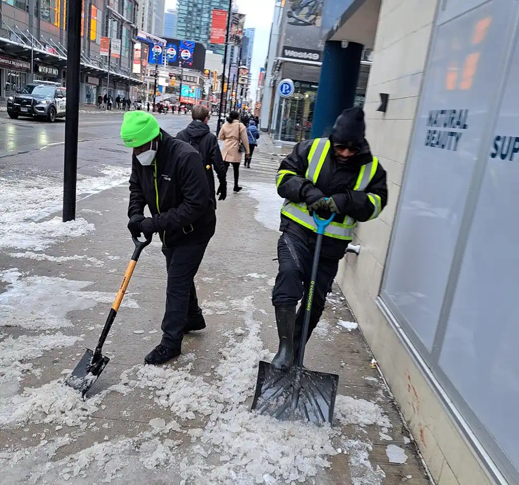 Two people with shovels clearing snow and ice from the sidewalk near Edward Street.