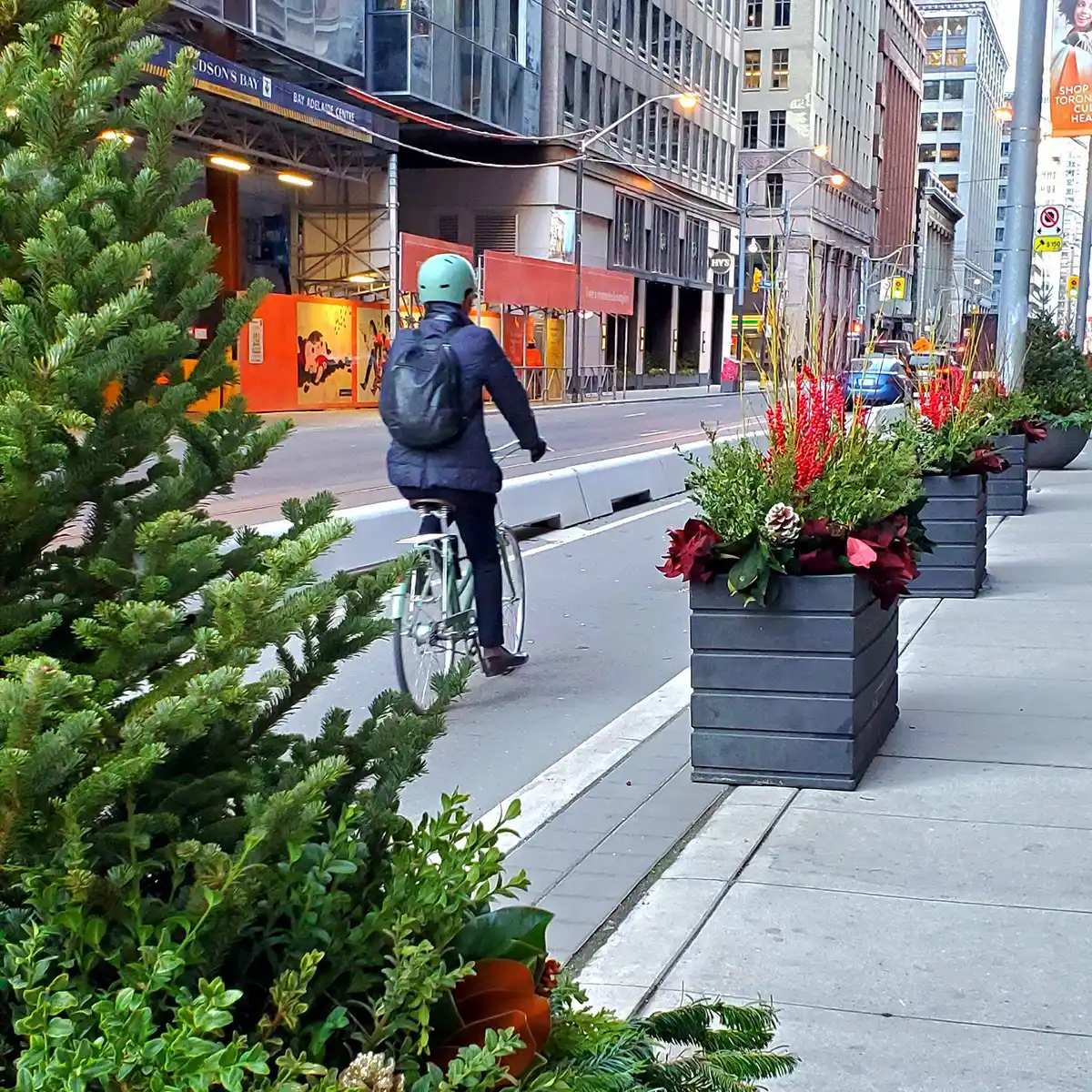 a person riding a bicycle on the street with a row of planters on the sidewalk